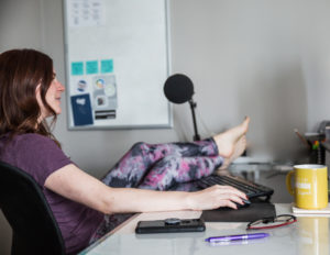 A woman sitting at a desk, focused on her work with her legs up on her desk in a relaxed position.