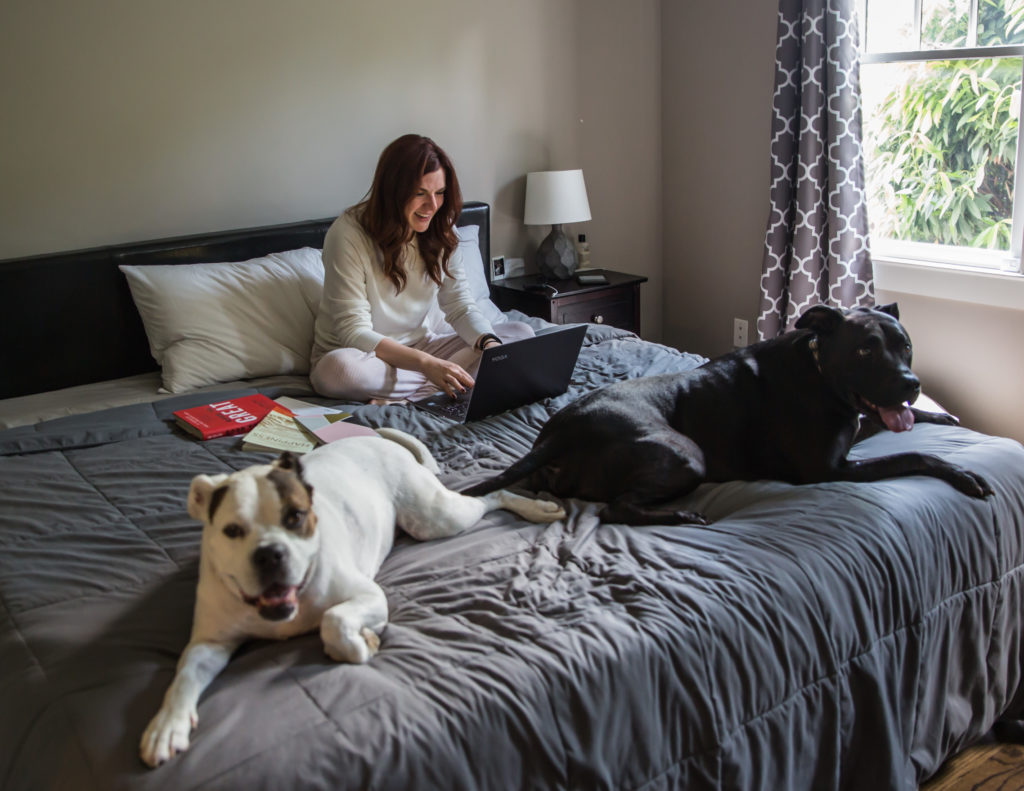 A woman sitting on a bed with two dogs, one medium and one large, looking content and relaxed.
