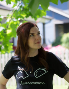 Woman in black shirt with "awesomeness" written on it, smiling confidently.