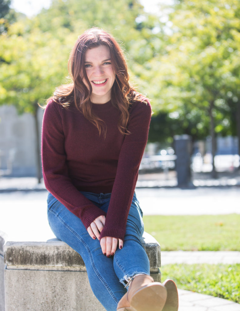 Anna-Vija, a red-headed woman sitting on a bench in a park.