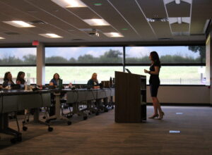 Anna-Vija McClain presents in front of an attentive audience in a conference room setting.