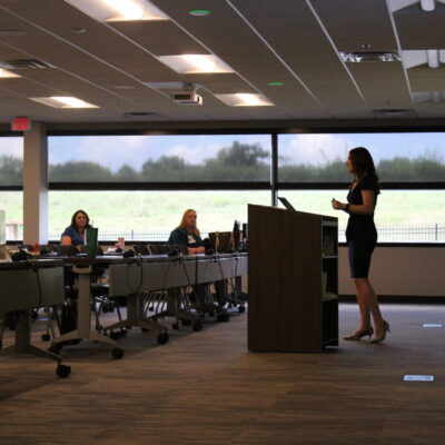 Anna-Vija McClain presents in front of an attentive audience in a conference room setting.