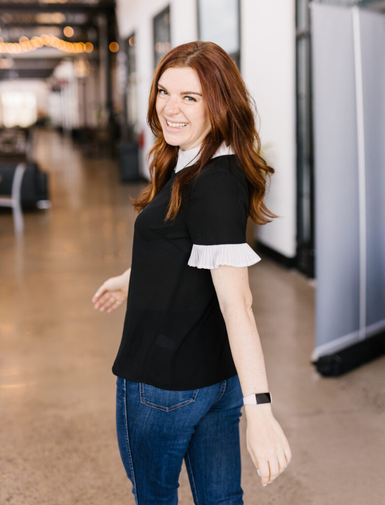 Anna-Vija McClain looks back to the camera with a smile. She is a pale woman with long red hair.