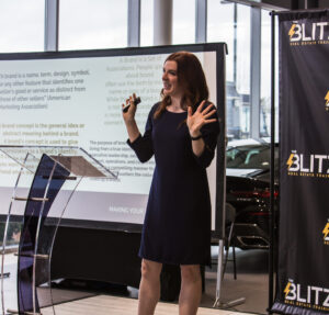 Anna-Vija McClain giving a talk in front of a large display, engaging the audience.