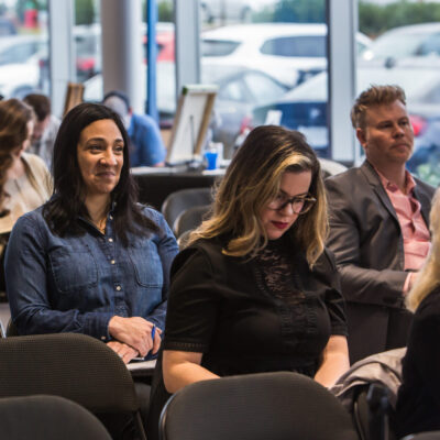 Engrossed audiences: a woman with a content smile looks on while another concentrates on taking notes during a professional seminar.