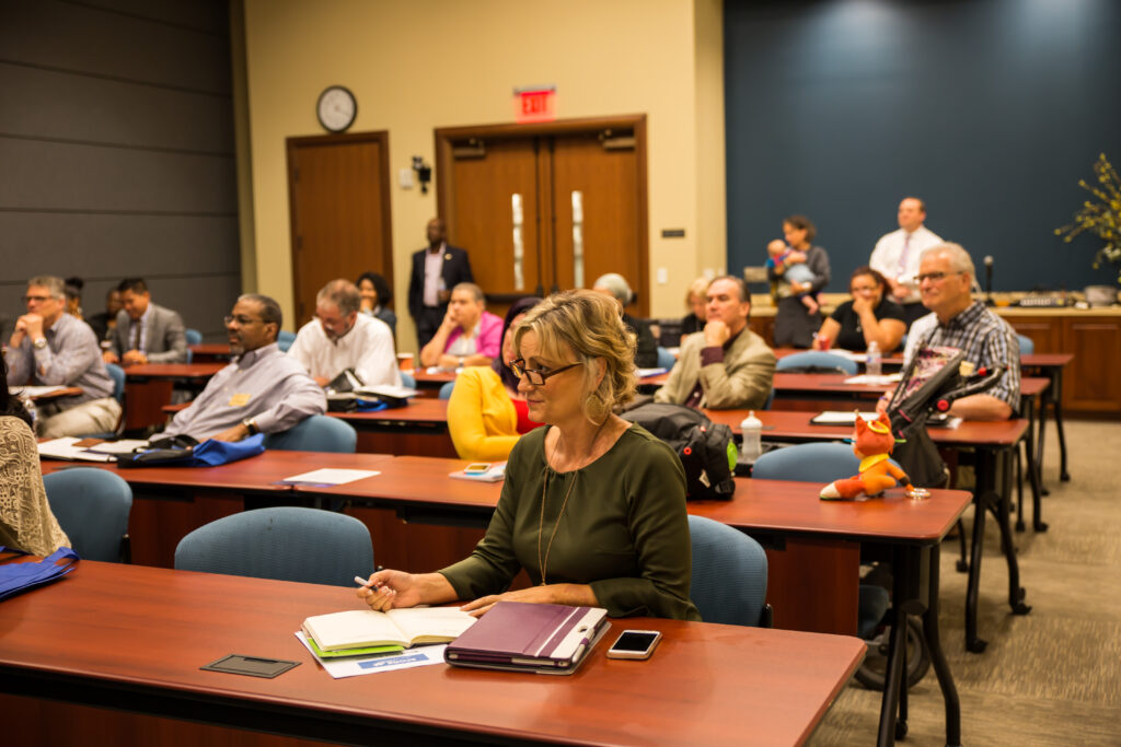 A group of attentive adult learners in a conference room setting, with notebooks ready for an educational seminar or lecture.